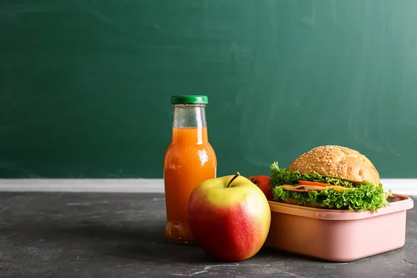 School lunch box with tasty food and bottle of juice on table