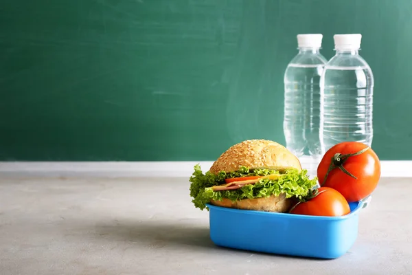 School lunch box with tasty food and bottles of water on table
