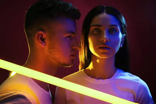 Portrait of young couple with neon lamp on dark background