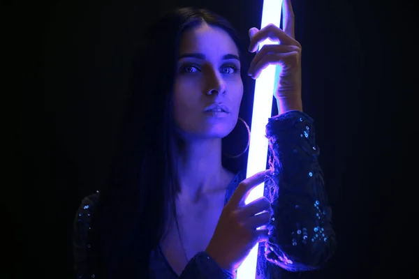 Portrait of beautiful young woman with neon lamp on dark background