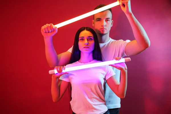 Portrait of young couple with neon lamps on color background