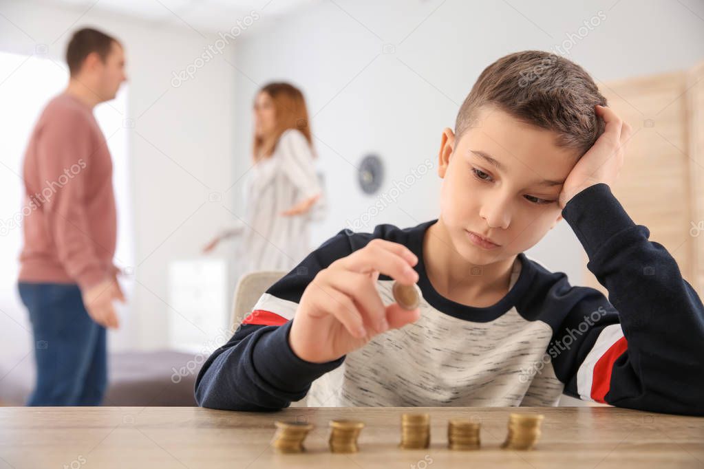 Sad little boy with coins and his quarreling parents at home. Concept of child support