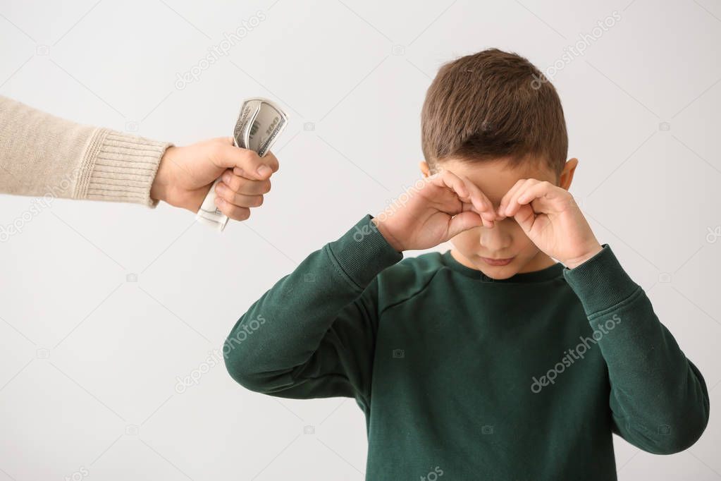 Sad little boy and male hand with dollar banknotes on light background. Concept of child support