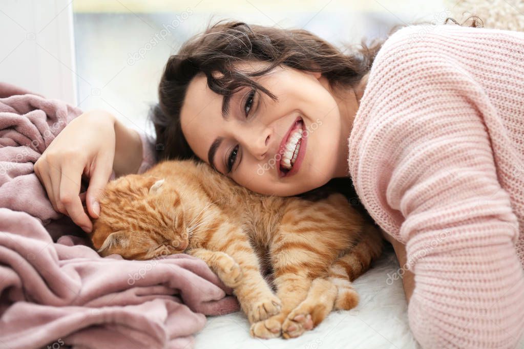 Young woman with cute funny cat near window