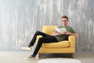Yakışıklı genç adam koltuk grunge duvarının yakınında oturan kitap okuma