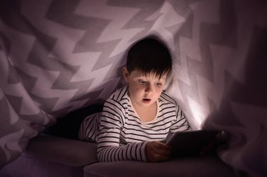 Battaniyenin altında çizgi film izlerken tablet bilgisayar ile şirin küçük çocuk