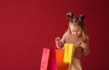 Sevimli küçük kız alışveriş torbaları içinde renk arka plan üzerinde seyir