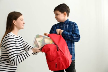 Anne koyarak öğle yemeği kutusu içine küçük oğlu okul öncesi ve sırt çantası