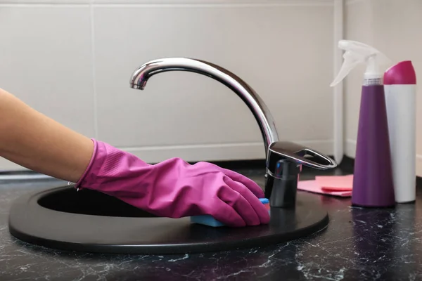 Young woman cleaning sink in bathroom