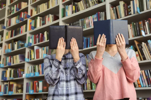 Young women hiding faces behind books in library
