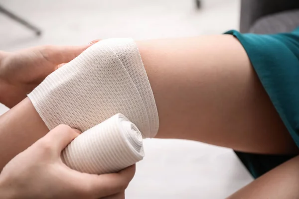 Woman applying bandage onto female knee, closeup