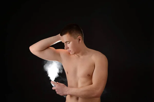 Handsome young man with deodorant on dark background