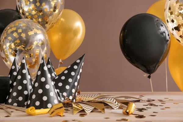 Balloons and party hats on table against color background