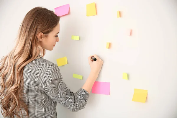 Woman writing on sticky notes attached to wall in office