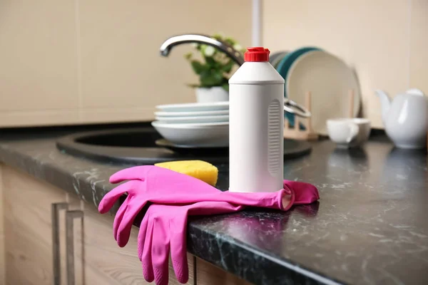 Bottle of detergent for washing dishes and rubber gloves near kitchen sink