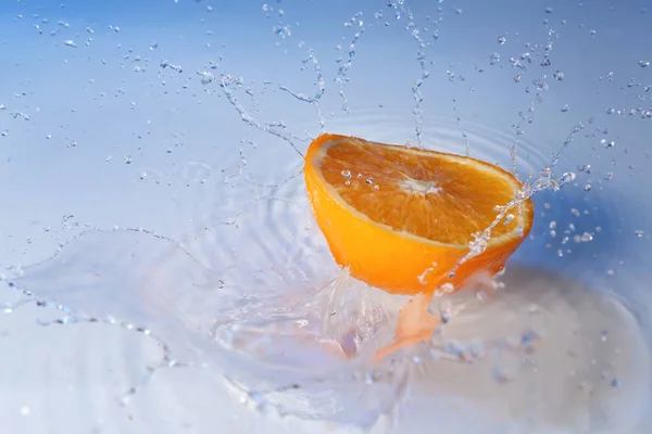 Ripe cut orange with water splash on color background