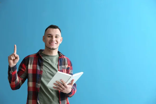 Schöner Junger Mann Mit Buch Und Erhobenem Zeigefinger Auf Farbigem — Stockfoto