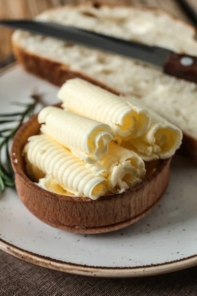 Bowl with butter curls and piece of bread on plate