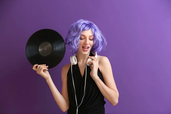 Beautiful young woman with vinyl disk and headphones on color background
