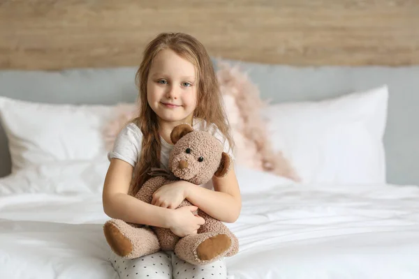 可爱的小女孩与玩具熊坐在床上 — 图库照片
