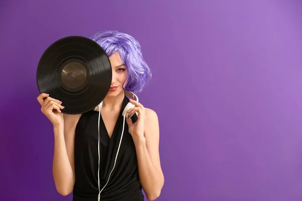 Beautiful young woman with vinyl disk and headphones on color background
