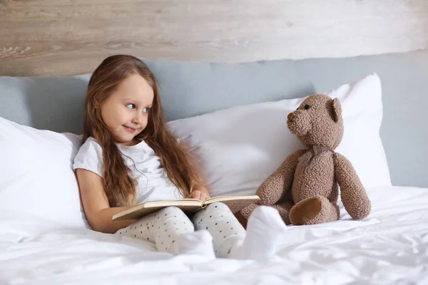 Aranyos Kislány Játék Medve Könyvével Ágyon Ülve — Stock Fotó