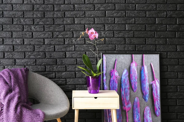 Table with beautiful orchid flower and armchair near dark brick wall