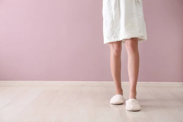 Young woman in slippers against color wall