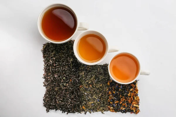 Cups with different types of tea and dry leaves on white background