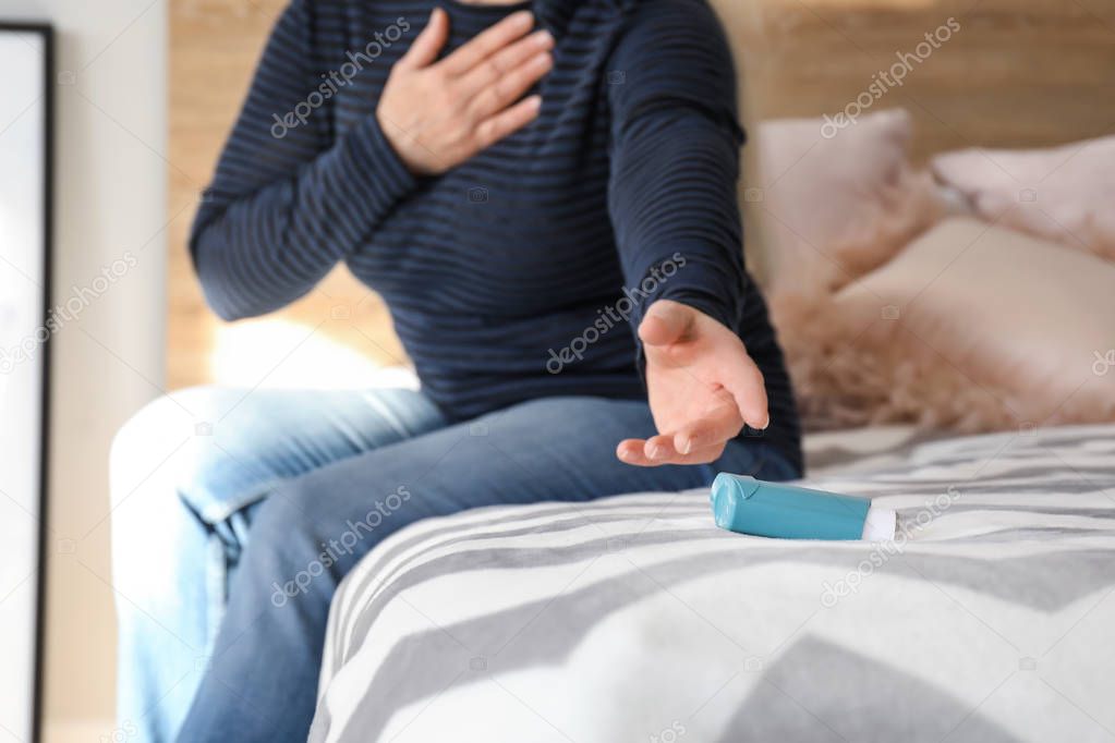Mature woman with asthma attack taking inhaler from bed