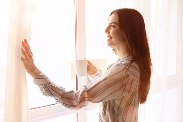 Morning of beautiful young woman with cup of coffee near window