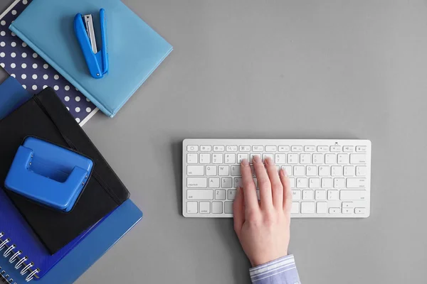 Female hand with computer keyboard and stationery on grey background