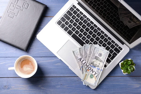 Laptop, money and paper with text ALIMONY on wooden table