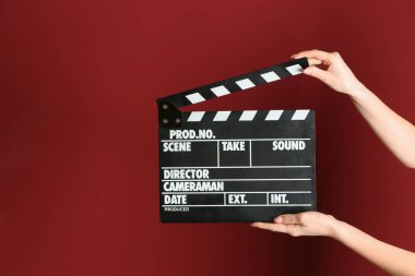 Female hands with cinema clapperboard on color background clipart