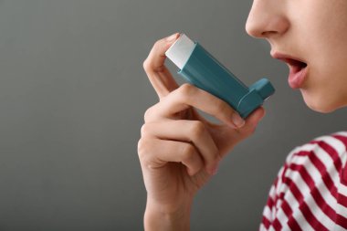 Gri arka plan üzerinde inhaler astım karşı kullanan genç kadın
