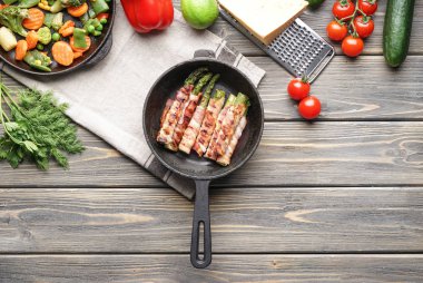 Ahşap masa üzerinde tavada kuşkonmaz lezzetli domuz pastırması ile kompozisyon sarılmış