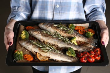 Woman holding baking sheet with cooked seabass fish and vegetables, closeup clipart