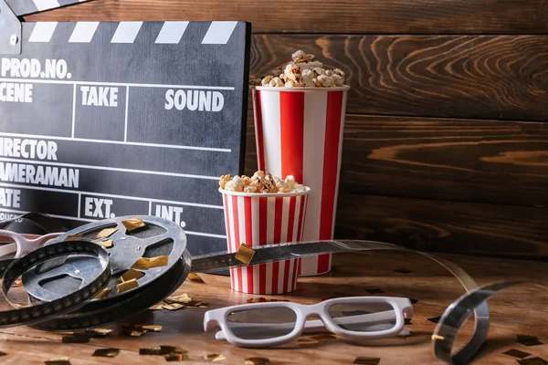 Movie clapper with film reel, popcorn and glasses on wooden table