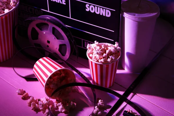 Movie clapper with film reel and popcorn on table