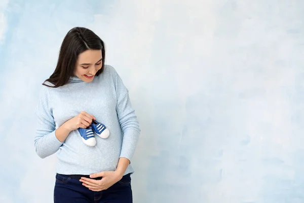 色の背景上のベビー シューズと美しい妊娠中の女性の肖像画 — ストック写真