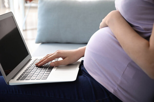 Beautiful pregnant woman using laptop at home, closeup