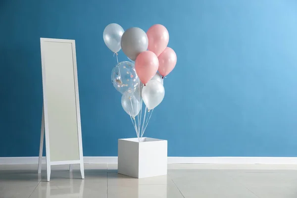Box with birthday balloons and mirror in room