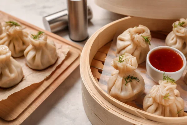 Bamboo steamer with tasty dumplings and sauce on table