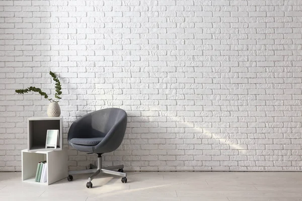 Comfortable armchair and shelf unit near white brick wall