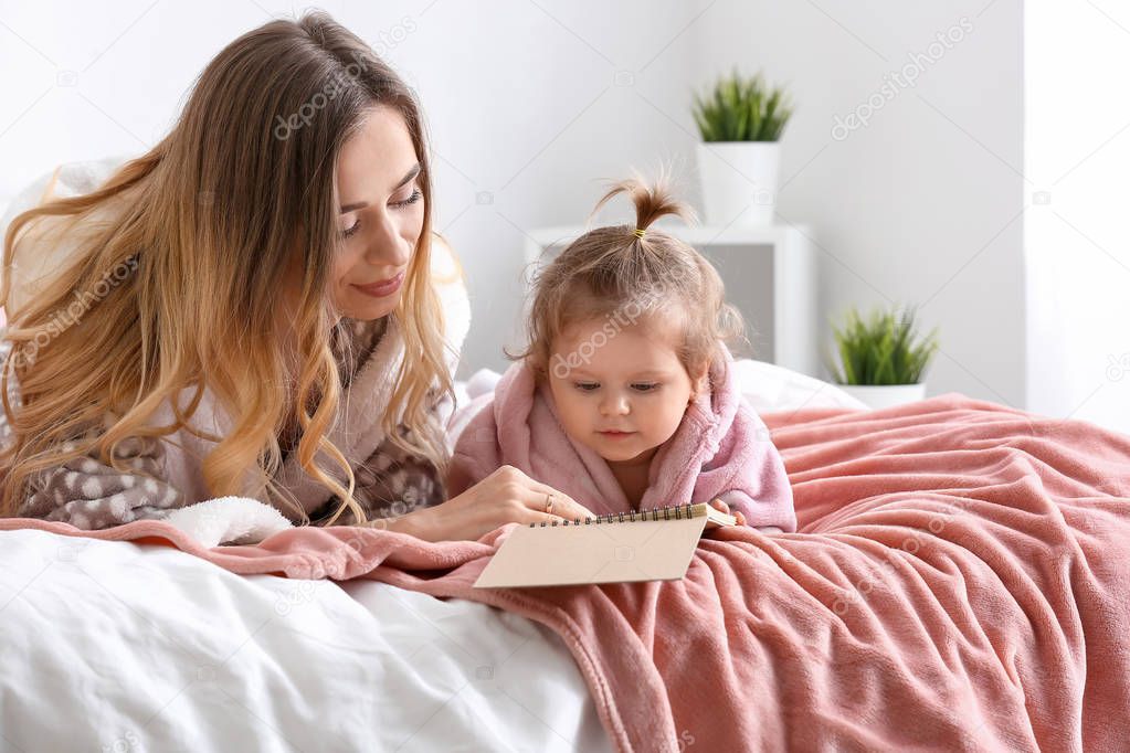 Young woman reading book to her cute little daughter at home