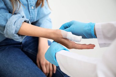 Doktor, genç bir kadının parmağına bandaj yapıştırıyor.