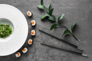 Plaka ile lezzetli suşi rulo, yosun ve gri masada yemek çubukları