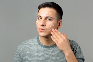 Gri arka plan üzerinde akne için uygulanan ilaç ile genç adam portresi