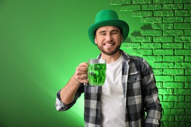 Yakışıklı genç adam yeşil şapkalı ve renk arka plan üzerinde bira kupa ile. Aziz Patrick günü kutlama
