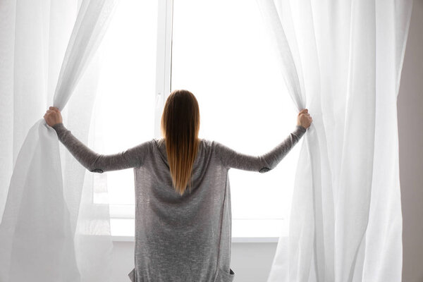 Young woman opening curtains in morning